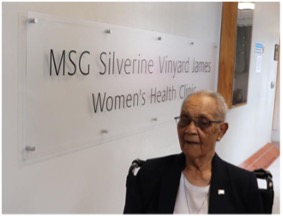 Photo of Silverine James standing beside the sign bearing her name inside the Salvem Virginia clinic